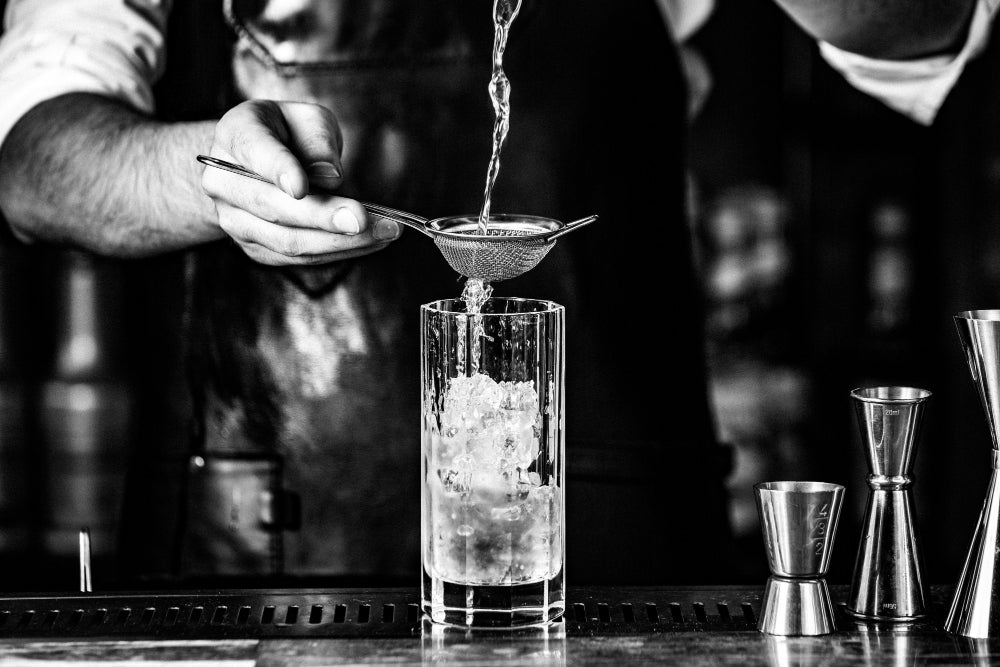 barista-putting-alcohol-into-cocktail-glass-with-syrup-ice-cubes
